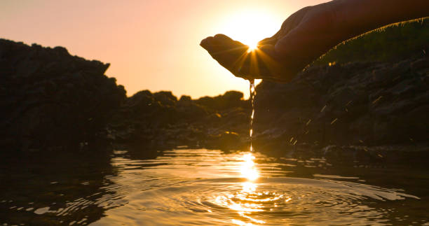 istock CLOSE UP, LENS FLARE: Sunbeams peep through a hand scooping water in sea puddle 2191039565