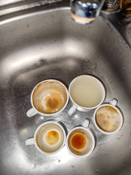 Used coffee cups with residue and stains in a metal sink under direct flash light