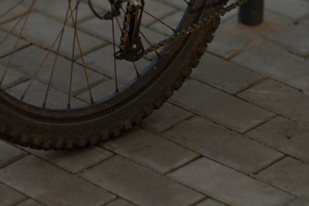 A bicycle wheel and chain are placed on a paved ground while various structures decorate the background