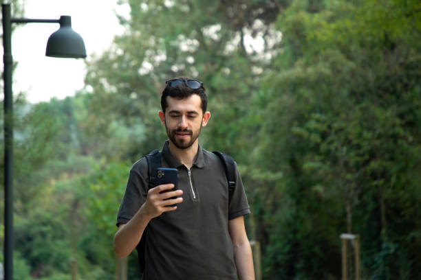 istock Young man looking at his phone while walking in nature 2191054831