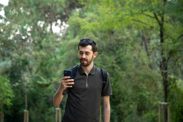 istock Young man looking at his phone while walking in nature 2191054891
