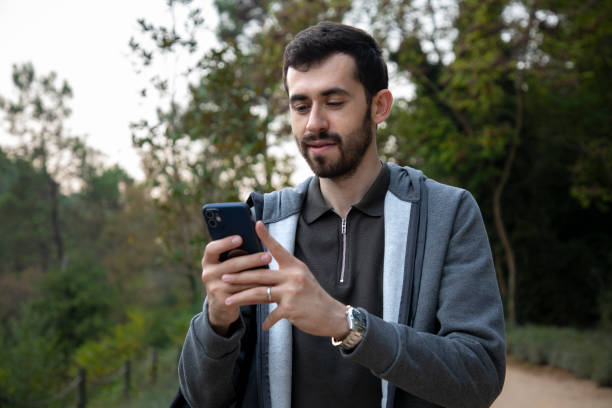 istock Young man looking at his phone while walking in nature 2191055131