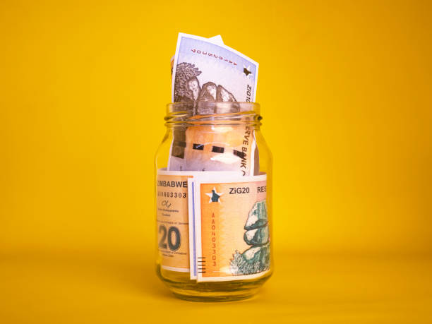istock Zimbabwean gold zig notes in transparent glass jar bottle container isolated yellow background. savings concept 2191058924