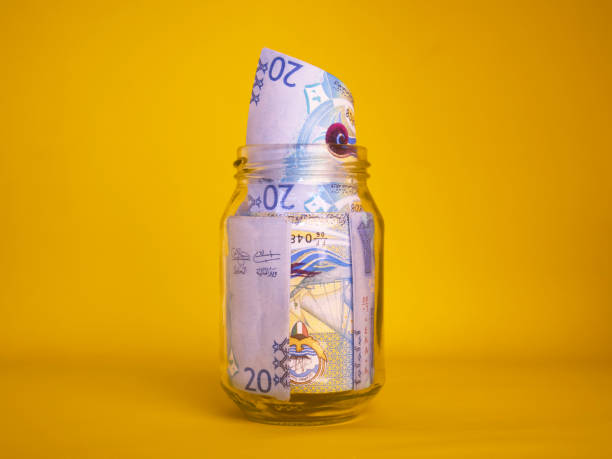 istock Kuwaiti dinar notes in transparent glass jar bottle container isolated yellow background. savings concept 2191058949