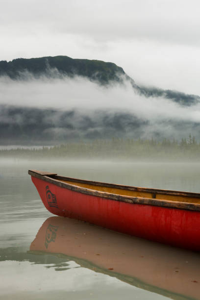 Tranquil serene nature scene of a foggy misty morning on Mendenhall Lake at the base of Juneau Icefield, with overcast clouds hiding the mountains and glacier beyond a red canoe in the water, Juneau, Alaska, USA