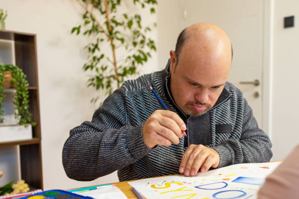 Mature male Student with Down syndrome painting in a classroom at the table