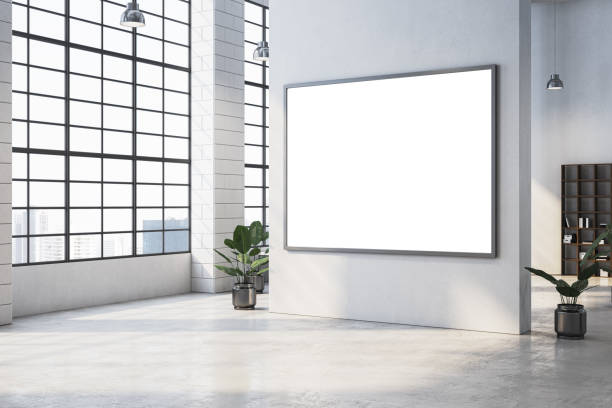 istock Modern open office space with large windows, plants, and a blank framed display on a white wall for branding or advertising. 3D Rendering 2191063705