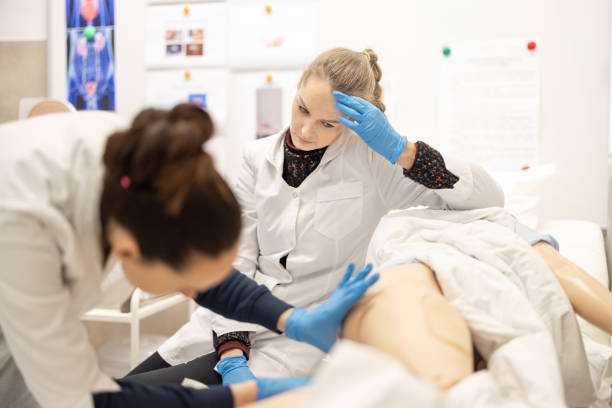 Focused healthcare students engage in hands-on learning activities during a medical training session, practicing clinical examination techniques on a life-sized model. Enema Procedure Training estudiantes de medicina que practican habilidades de examen en un modelo de entrenamiento con enfoque serio. enfermera practicante de atención médica que demuestra atención al paciente. universidad. capacitación sobre el procedimiento de enema