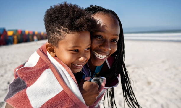 Smiling mother and son wrapped together in a towel on beach Smiling mother and son wrapped together in a towel on a beach during a summer vacation woman wrapped in bath towel stock pictures, royalty-free photos & images