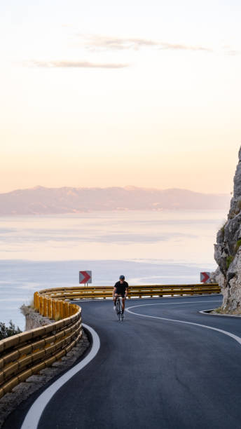 istock Road biker rides up curving mountain road 2191087544