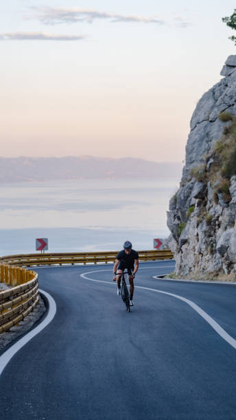 istock Road biker rides up curving mountain road 2191087564