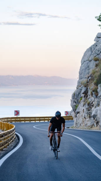 istock Road biker rides up curving mountain road 2191087567