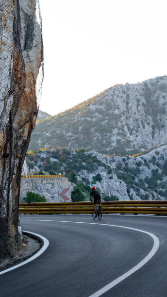 istock Road biker rides up curving mountain road 2191087592