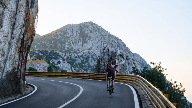 istock Road biker rides up curving mountain road 2191087598