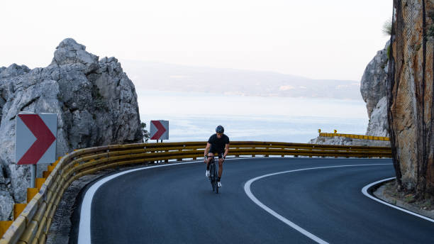 istock Road biker rides up curving mountain road 2191087627
