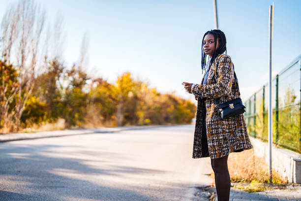 istock Young black woman using mobile phone standing next to a road. 2191104830