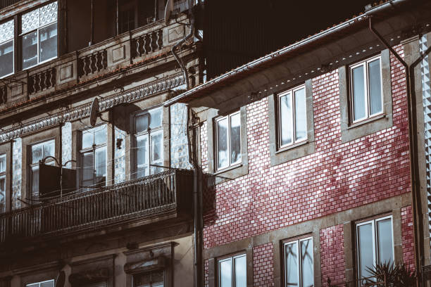 A close-up of traditional Portuguese residential buildings featuring intricate iron balconies, detailed tile facades, and red brick walls reflecting strong sunlight in urban settings