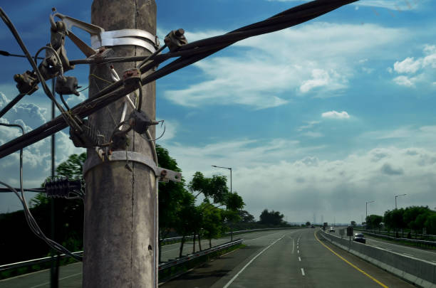 an electric pole with chaotic strands of cables and wires against the backdrop of a toll road on a day with a clear sky