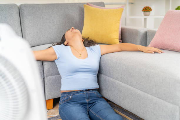 istock Young woman feeling hot at home using an electric fan 2191114167