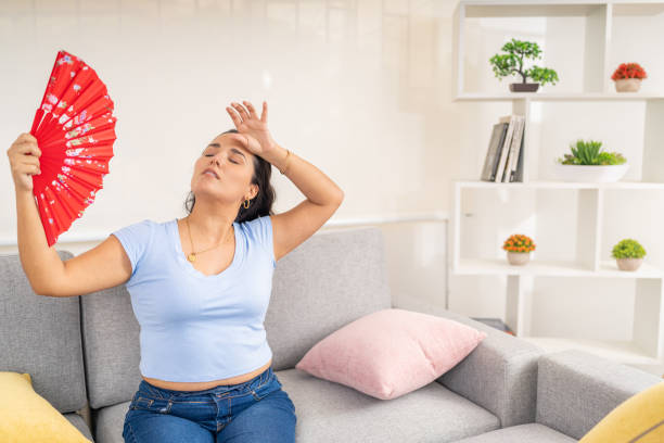 istock Woman feeling heatstroke waving a fan on sofa 2191114202