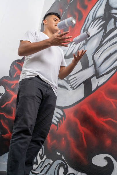 istock Young artist juggling spray cans in front of mural 2191120165