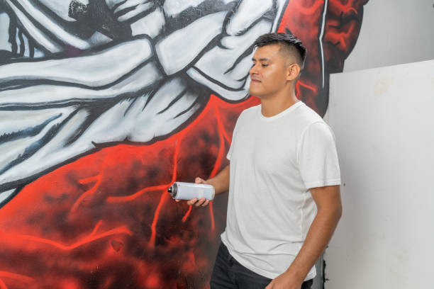 Muralist concentrating while holding a spray paint can, adding details to a vibrant artwork on a red wall