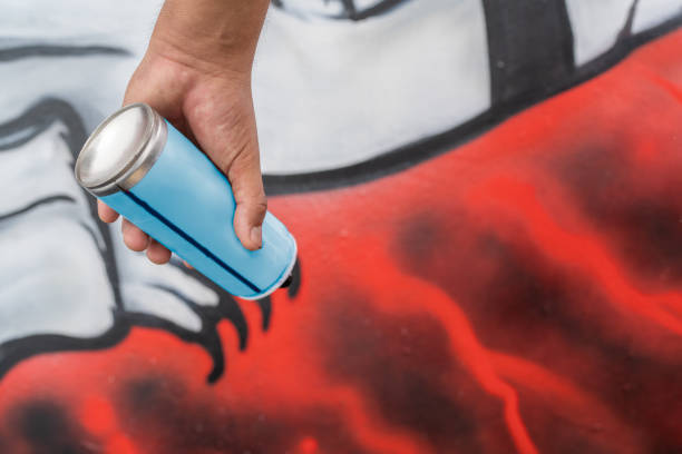 Street artist's hand holds a spray paint can, adding vibrant colors to a developing mural on a wall