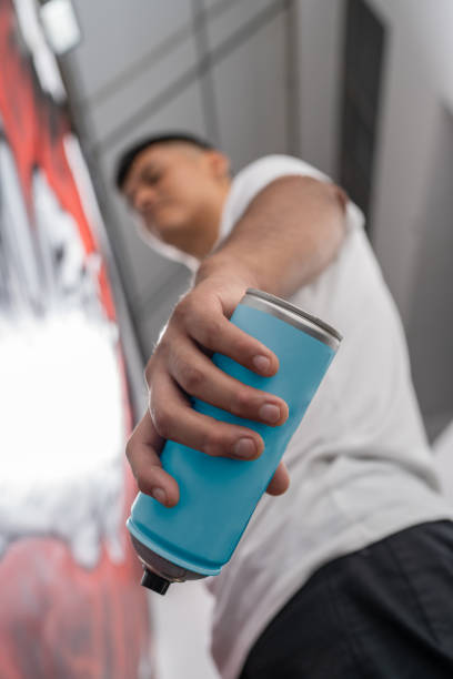 Young street artist holding a spray paint can, creating a vibrant mural on a wall, showcasing urban art and creativity