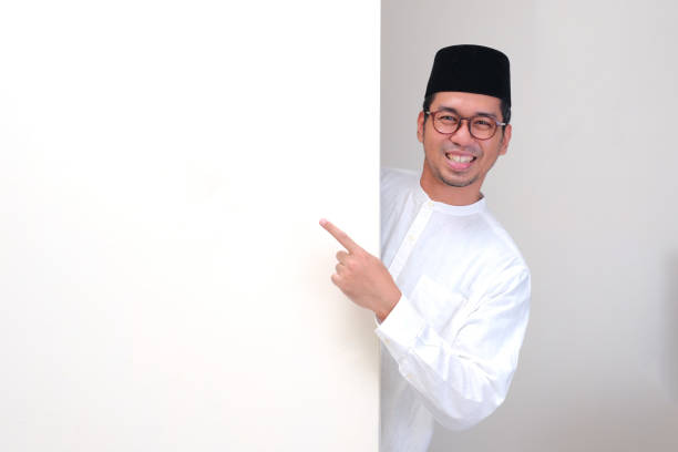 istock A muslim man peeking out behind wall smiling and pointing at it 2191128124
