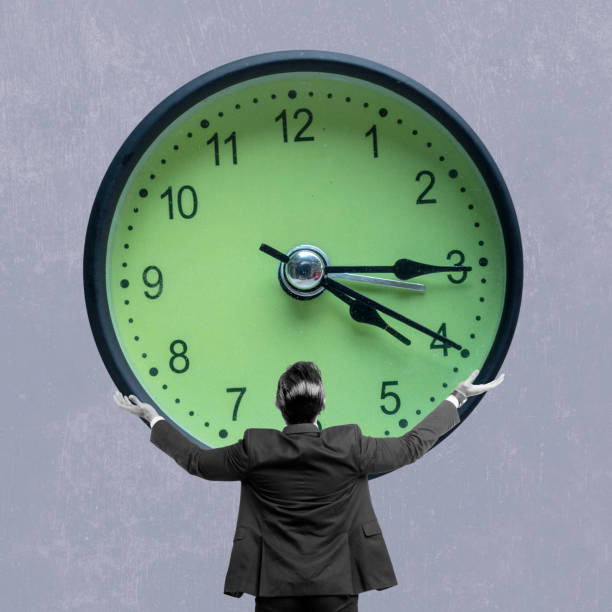 istock Rear view of a businessman holding a clock on a colored background 2191128289