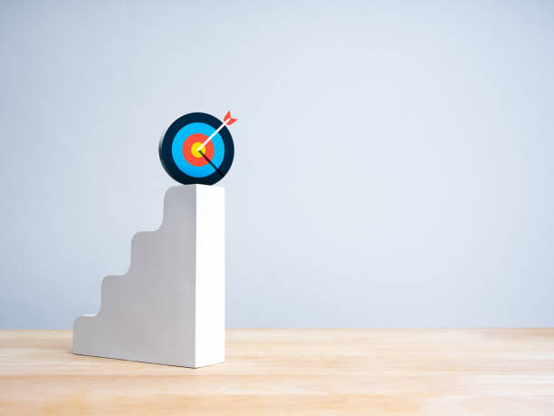 istock Modern colorful target icon on top of white 3d bar graph chart steps on wood table, white background with copy space. Business growth process, profit and investment, leadership success plan concepts. 2191129207