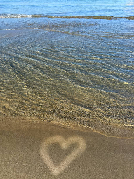 Sea soft waves on the beach with a heart drawn on the sand.