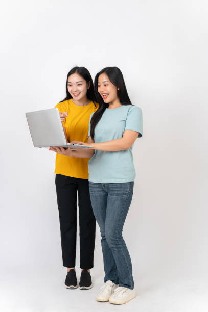 istock Two happy Asian women standing against a white studio background, looking at something on a laptop. 2191146421