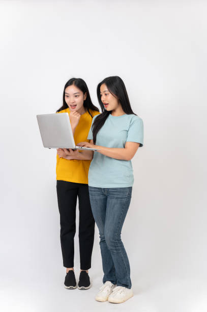 istock Two excited Asian women standing against a white studio background, looking at something on a laptop. 2191146426
