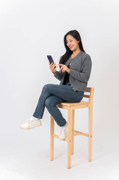 istock An attractive Asian woman sits on a chair on a white studio background, enjoys using her smartphone. 2191146467