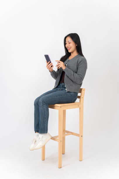 istock An attractive Asian woman sits on a chair on a white studio background, enjoys using her smartphone. 2191146479