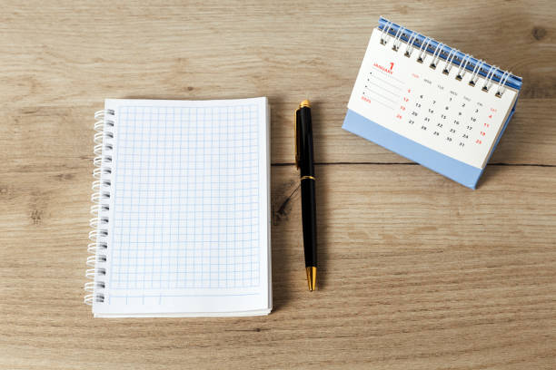 A desktop calendar for 2025, a ballpoint pen and an open notebook on the desk.