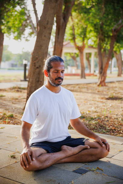 istock Indian man sitting cross-legged on ground in public park and practicing yoga 2191148616