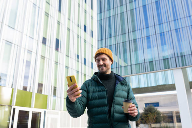 istock Smiling young man using smartphone and holding coffee outside office building 2191148989