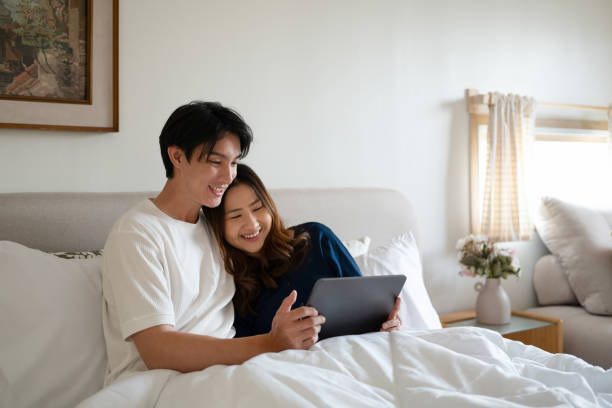 cặp đôi người lớn yêu thương sử dụng máy tính bảng kỹ thuật số dưới chăn ấm trong phòng ngủ ấm cúng - ảnh cưới hình ảnh sẵn có, bức ảnh & hình ảnh trả phí bản quyền một lần