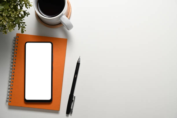 istock Smartphone with blank screen, notebook, cup of coffee and pen on white table 2191152541