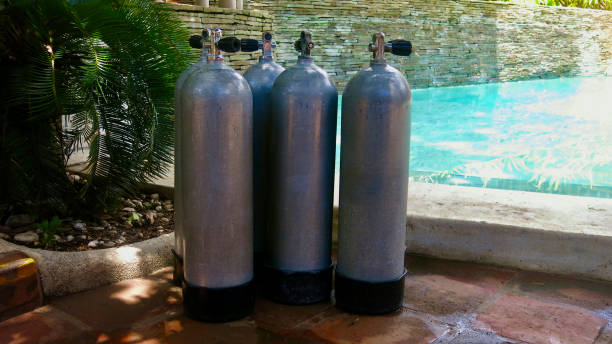 Five diving tanks stand in the shade under a tree near the pool.
