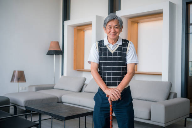 Portrait of a cheerful and stylish elderly Asian man standing in a modern living room at home.