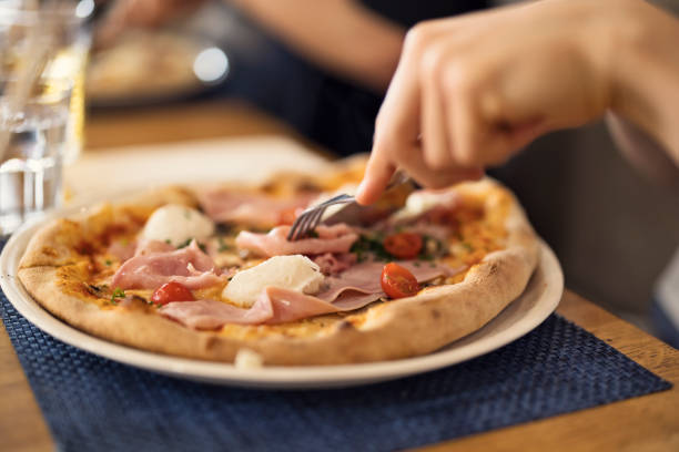 Multi generation family enjoying eating a meal together in a restaurant. Closeup of a teenage boy eating fresh pizza with ham and  mozzarella.Shot with Canon R5