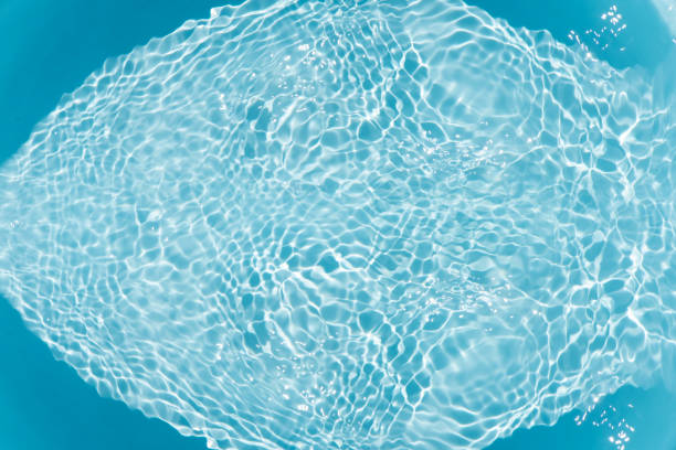 Blue water with ripples on the surface. Defocus blurred transparent blue colored clear calm water surface texture with splashes and bubbles. Water waves with shining pattern texture background.