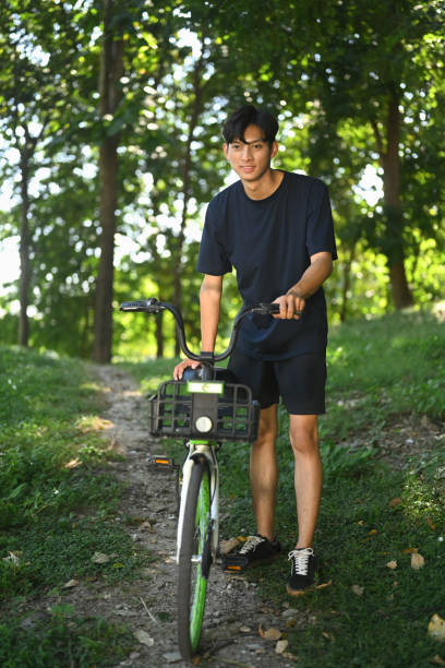 istock Young asian man pushing his bicycle walking through forest path on a beautiful sunny day. 2191153939