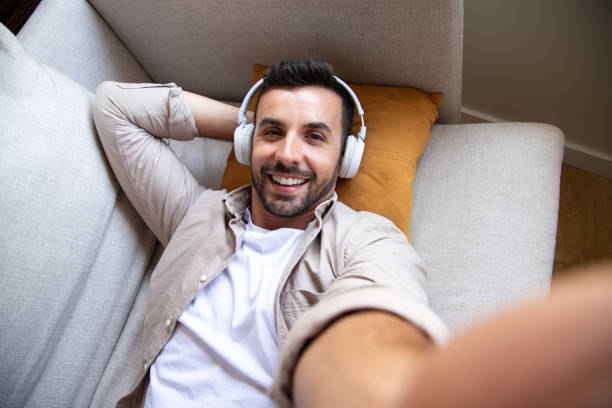 istock Young man relaxing on sofa taking a selfie while listening to music 2191155419