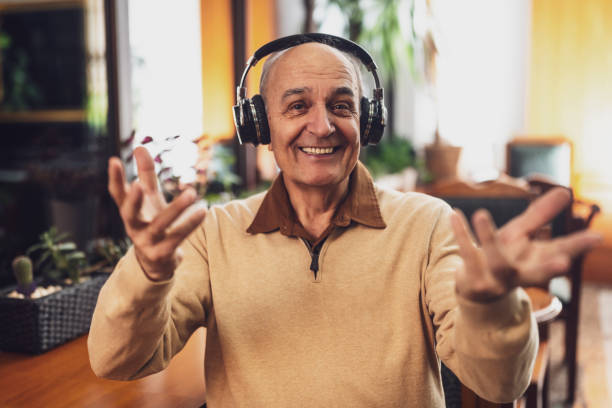 istock Smiling senior man with headphones looking at camera and gesturing while having a video call 2191161066