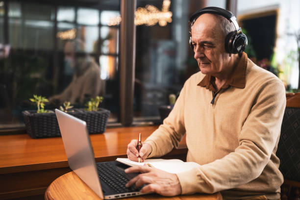 istock Elderly man with headphones using laptop and studying online in cafe 2191161093