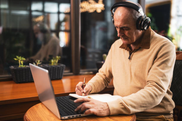 istock Older man with headset and laptop learning online in cafe 2191161154